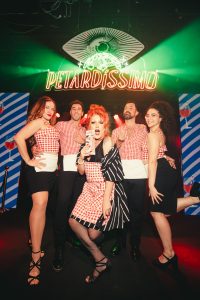Camareros y una artista drag posando bajo el neón de Petardíssimo en LuLa The Club